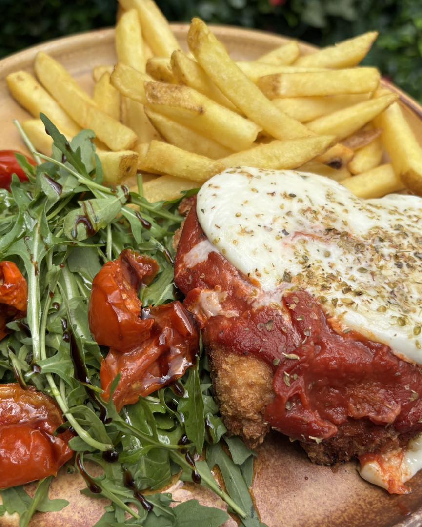 Chicken parmigiana: breaded chicken baked with fresh mozzarella, tomato passata, basil, rocket and cherry tomato salad, served with fries 